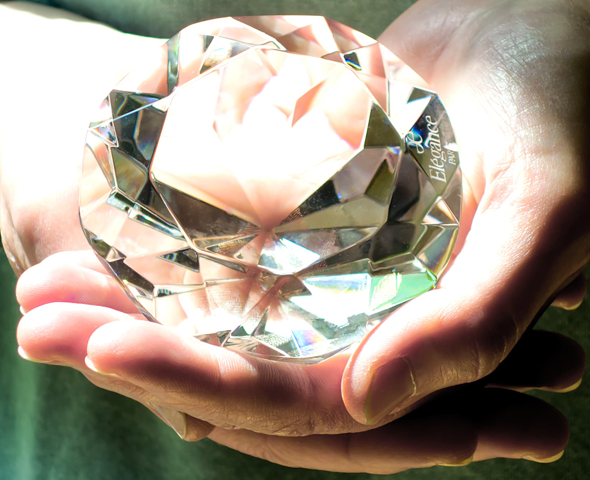 Großer leuchtender facettierter Glaskristall von zwei Händen gehalten.